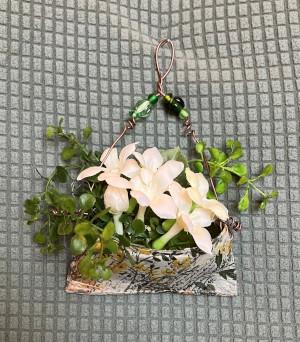 A handing pocket made from a tin can with fake greenery and flowers