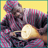 Man in red and blue striped clothing with hat holding a drum