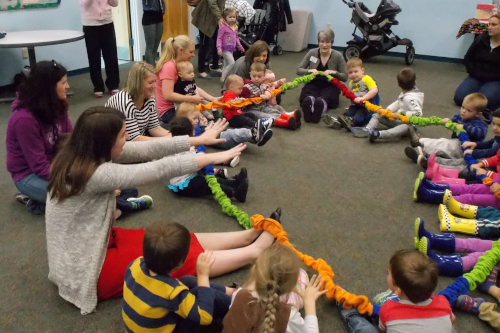 photo of a group of children and adults sitting in a circle holding a rope